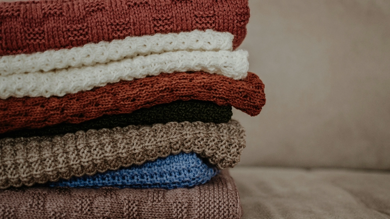 A stack of folded knitted sweaters in assorted colors displayed on a sofa.
