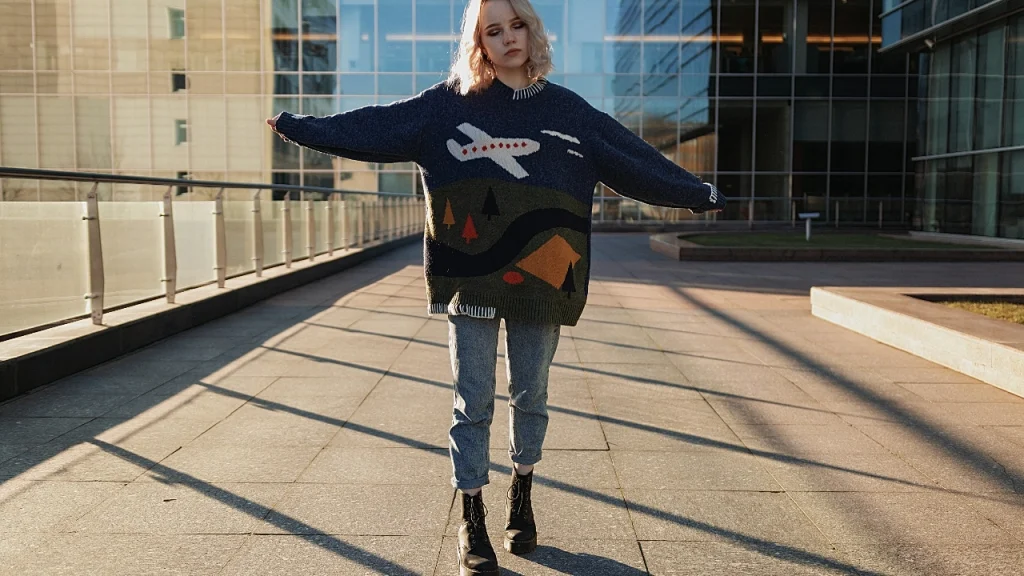 A woman wearing an oversized graphic sweater while standing in a modern city plaza.