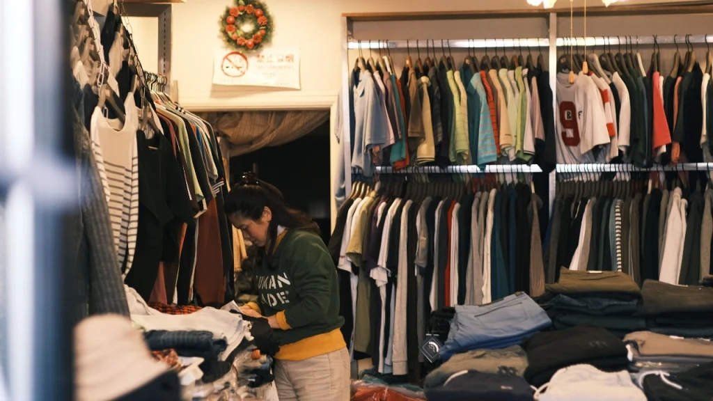 A clothing store interior with racks of garments and folded apparel on display tables.