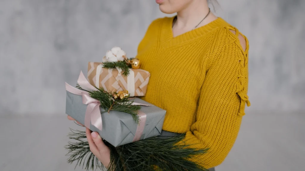 Woman wearing a mustard knit jumper while holding wrapped Christmas gifts