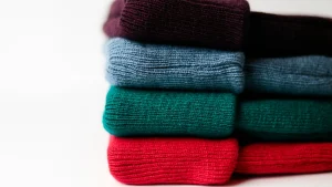 Wholesale knitted sweaters production tools with scissors, crochet hooks, yarn, and textured knit fabric.