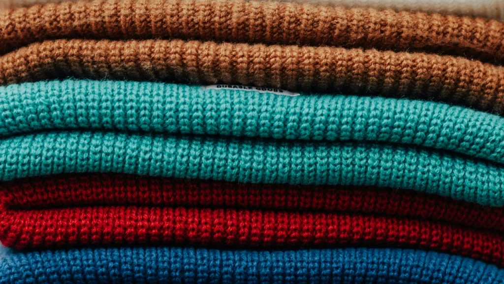 Wholesale knitwear stack of colorful folded sweaters showing fabric texture and bulk color options.