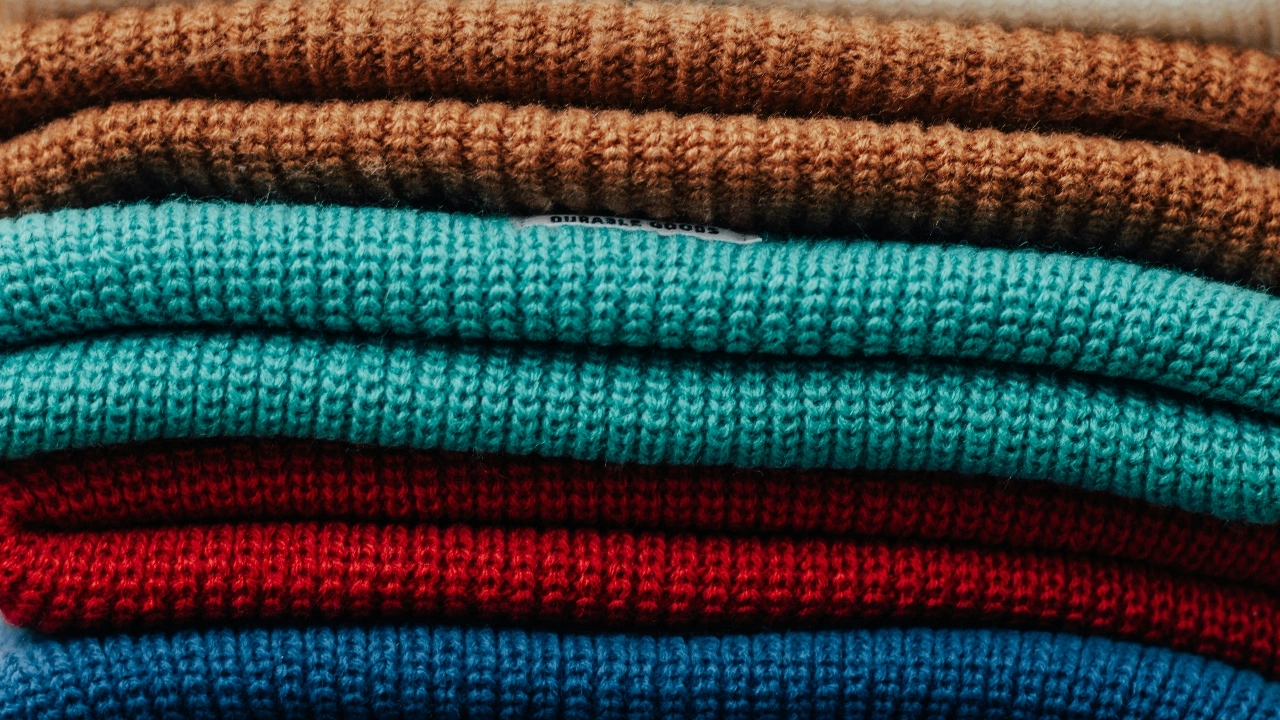Wholesale knitwear stack of colorful folded sweaters showing fabric texture and bulk color options.