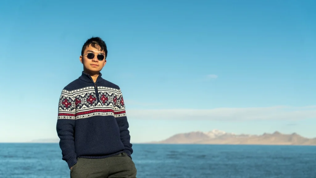Zip cardigan style knit sweater with patterned chest design worn by a man near the ocean.