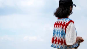Person wearing a colorful argyle Sleeveless Knitwear vest layered over a white T-shirt outdoors.