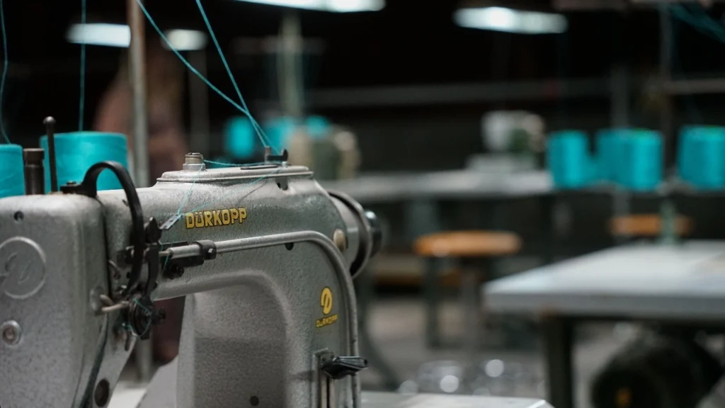 Industrial sewing machine with blue threads inside a sweater factory production area.