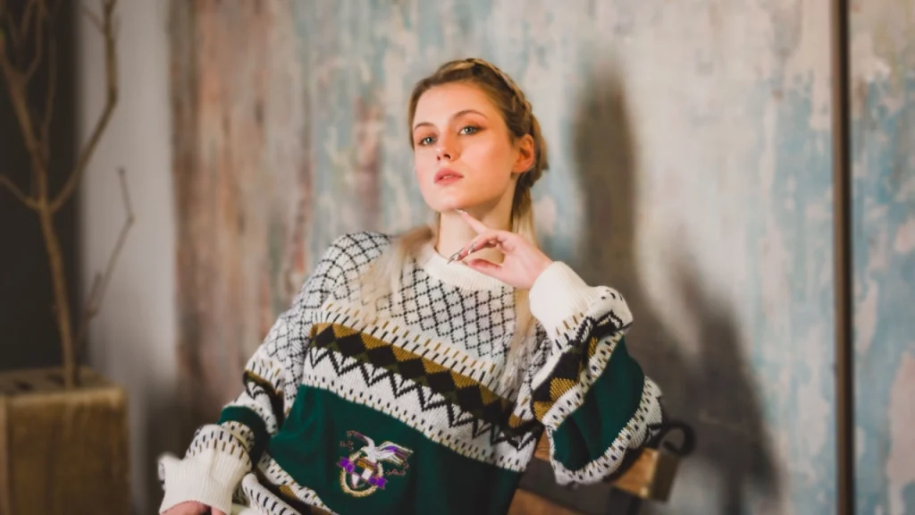 Model wearing a patterned custom sweater with fair isle details and an embroidered-style chest graphic indoors.