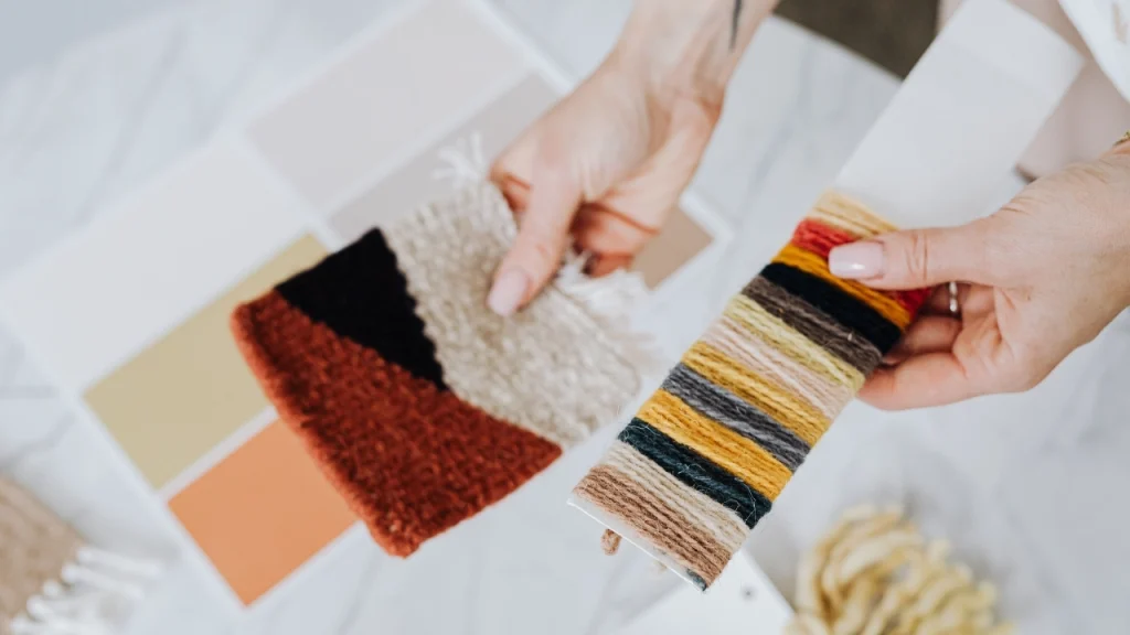Hands comparing knit swatches and yarn cards for pre production sample approval.
