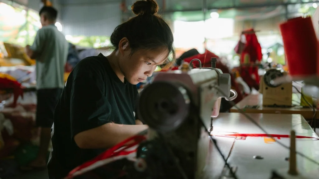 Worker sewing fabric on an industrial machine inside a sweater factory workshop.