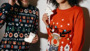 Two people wearing colorful custom sweaters with Christmas graphics while holding festive cookies.