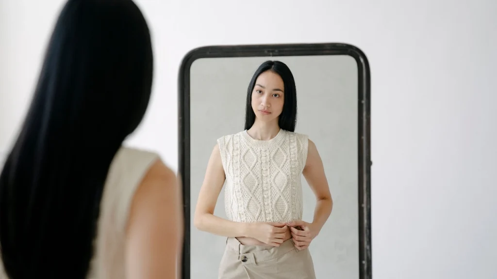Woman wearing a cream cable knit Sleeveless Knitwear vest in front of a mirror.