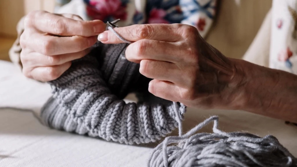 Close-up of hands knitting a gray Custom Knitwear piece with yarn and needles.