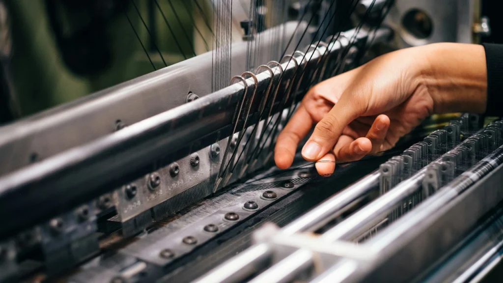 Worker adjusting threads on a knitting machine during Knitwear Production.
