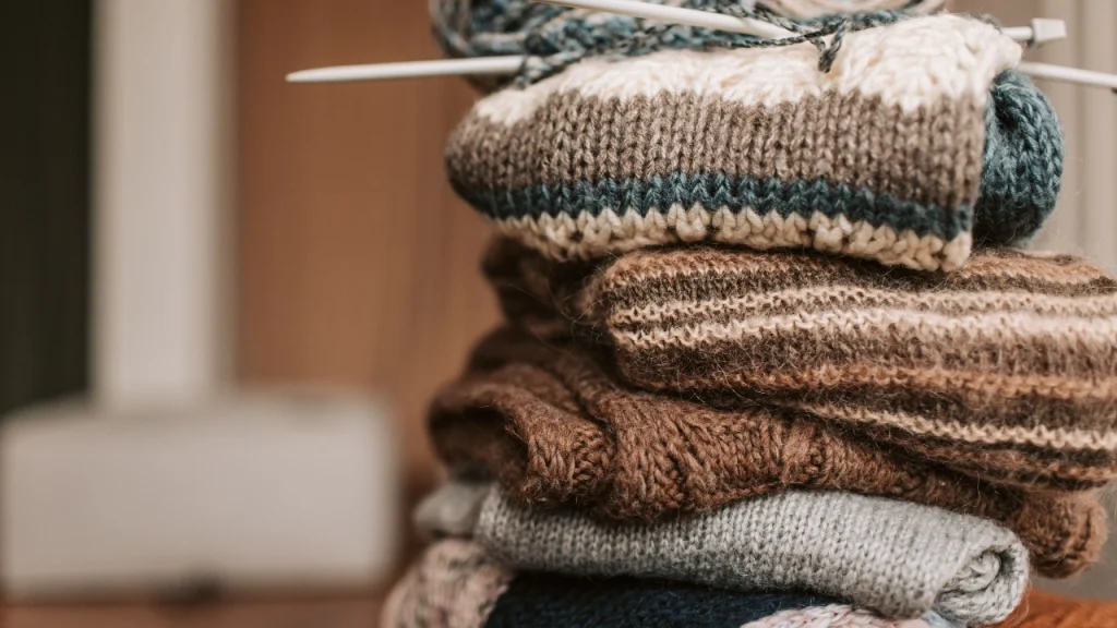 Stack of textured knit sweaters for knitwear supplier product development.