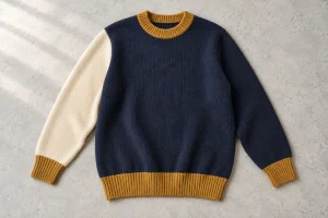 Navy pullover with one cream sleeve and ochre rib trims on a pale surface