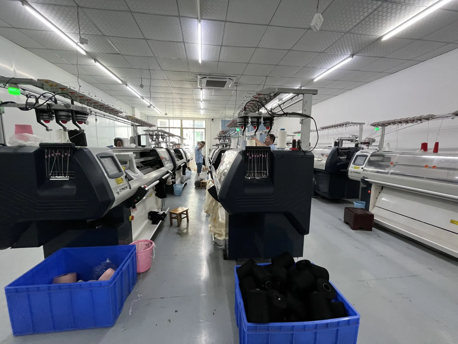 Row of flat knitting machines with knitted panels collected in bins