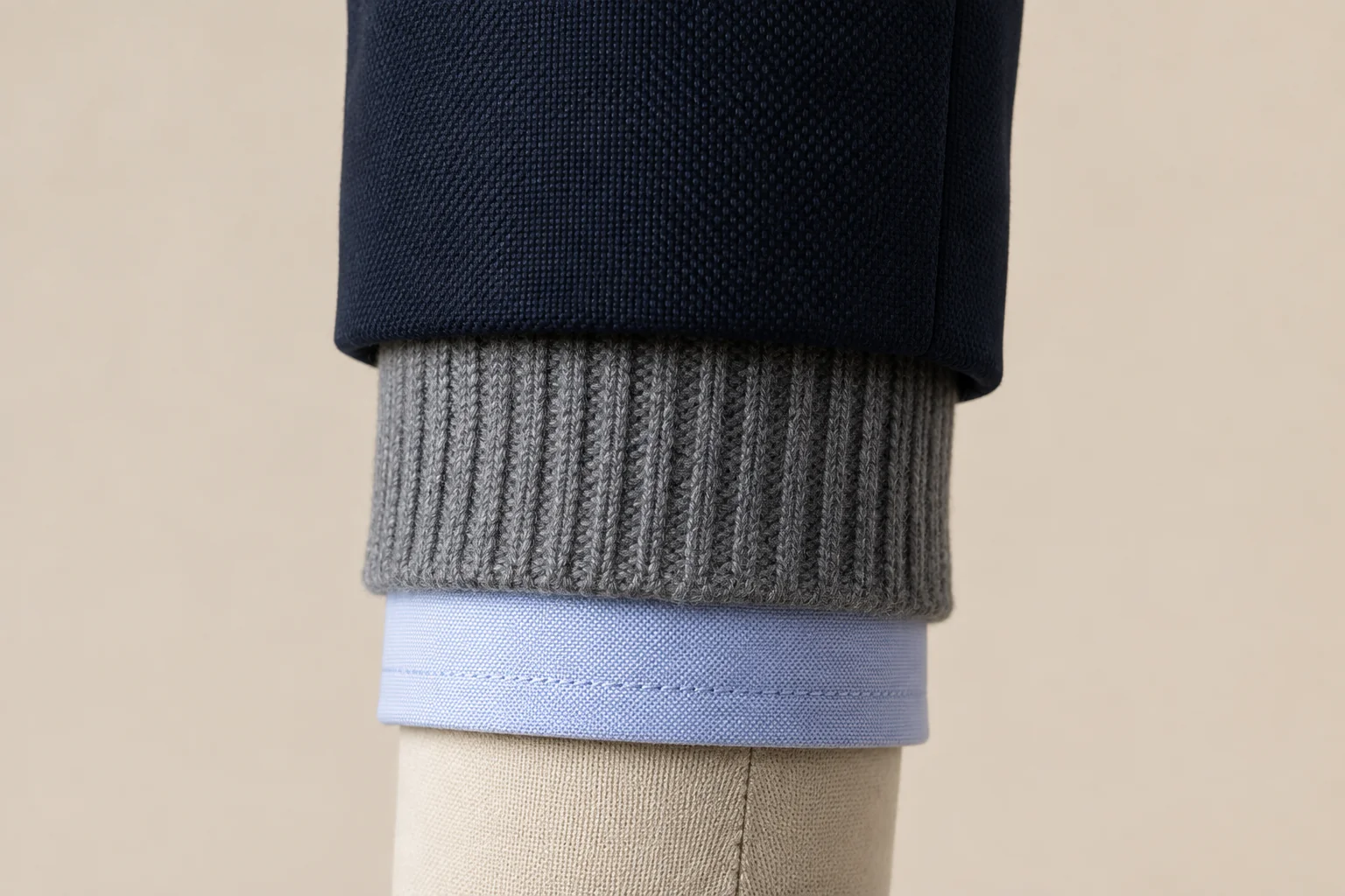 Close view of a navy blazer sleeve, gray knitted rib cuff and pale blue shirt cuff on a dress form.