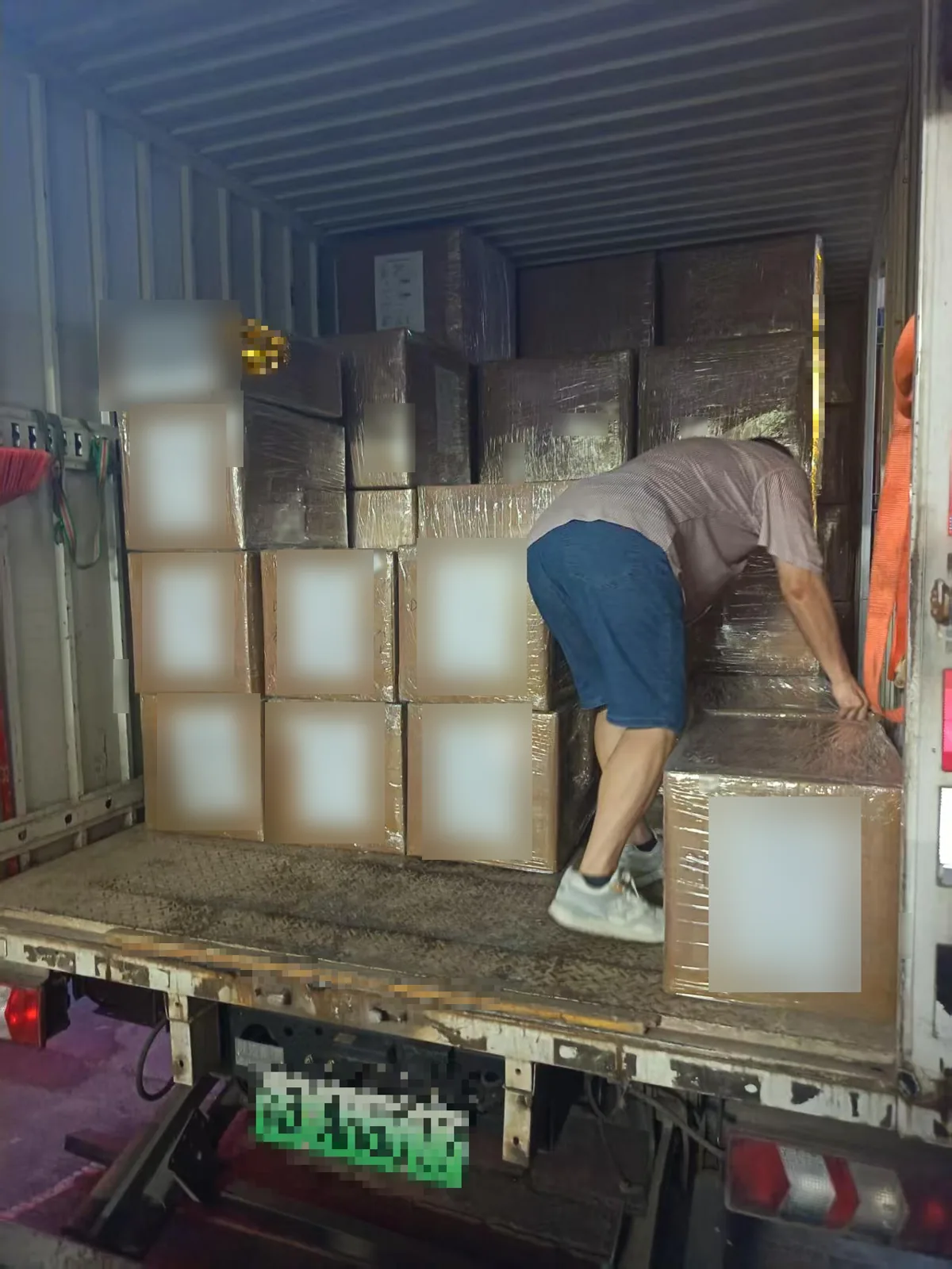 Worker loading stretch-wrapped knitwear cartons into a delivery truck